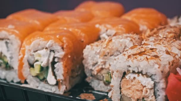 棒は寿司箱に1本の寿司を入れ 閉じます プラスチック製の箱の中で転がる デリバリーコンテナに様々なおいしい寿司ロールの日本語セット コンセプト健康的な食事 アジア料理 テイクアウト食事 — ストック動画