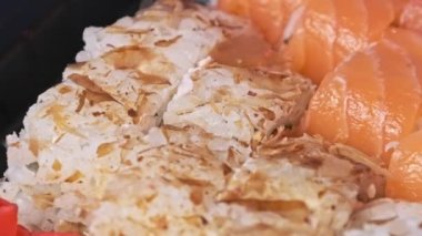 Suşi plastik bir kutuda yuvarlanır ve yakın plan çekilir. İçinde taze Japon dürümleri, zencefil ve vasabi olan suşi kutusu teslimat plastik bir kapta dönüyor. Asya yemekleri, paket yemek, sağlıklı yemek.