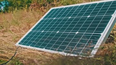 Taşınabilir güneş paneli doğada yatar ve kamplarda turistler için enerji üretir. Güneşli bir yaz gününde çimen üretim gücü üzerine bir güneş fotovoltaik panelinin yakın çekimi.