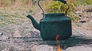 Tütsülenmiş çaydanlık, yerdeki taşlardan yapılmış kendi kendini yetiştirmiş turist ocağının üzerinde kaynar su. Doğada bir turist kamp ateşinin üzerinde duran eski bir çaydanlık. Ormanda şenlik ateşinde çay yapmak.
