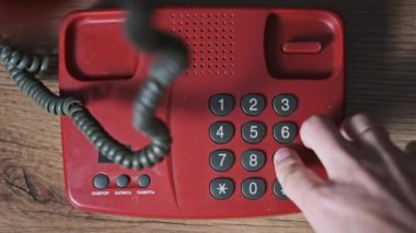 911 'i arıyorum. Eski bir kırmızı telefonun üst görüntüsü, erkek eli tuşlara basar. Eski bir ev telefonundan acil durum numarasını arıyorum. Retro tuşlu numara tuşları. Yakın plan.