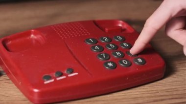 911 'i arıyorum. Eski bir kırmızı telefonda, bir adam tuşlara basar. Eski bir ev telefonundan acil durum numarasını arıyorum. Retro tuşlu numara tuşları. Yakın plan.