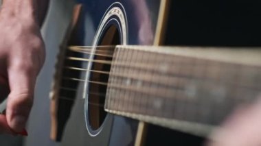 Genç adam evde akustik gitar çalar. Oturma odasında kanepede oturan müzisyen gitarı. Şarkı çalmayı öğrenmek, telleri tıngırdatmak, akorlar çalmak. Yavaş Hareket, yaşam tarzı, akıl sağlığı.