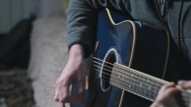 Genç adam evde akustik gitar çalar. Oturma odasında kanepede oturan müzisyen gitarı. Şarkı çalmayı öğrenmek, telleri tıngırdatmak, akorlar çalmak. Rahatlatıcı, yaşam tarzı konsepti, akıl sağlığı.