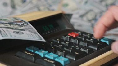 Dolarlarla çevrili eski bir hesap makinesine güveniyoruz. Yakın plan. Tahta masadaki eski hesaplama makinesinin klavye tuşlarına erkek eli basar. Konut finansmanı, para birimi, tasarruf, mali faturalar
