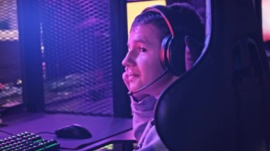 Esport kulübündeki genç bir çocuk oyun sandalyesinde monitörün önünde oturup atış oyunu oynuyor. Bilgisayar kulübünde kulaklık takan bir genç bir video oyununa odaklanıyor, arkadaşlar çevrimiçi turnuva oynuyor