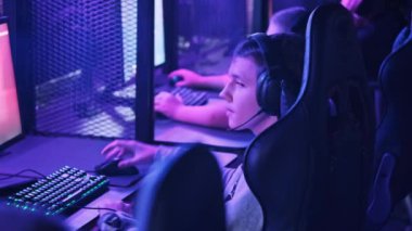 Esport kulübündeki genç bir çocuk oyun sandalyesinde monitörün önünde oturup atış oyunu oynuyor. Bilgisayar kulübünde kulaklık takan bir genç bir video oyununa odaklanıyor, arkadaşlar çevrimiçi turnuva oynuyor