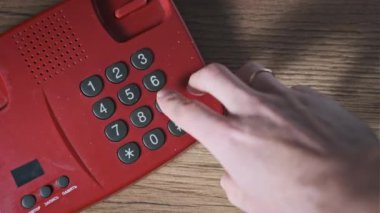 911 'i arıyorum. Eski bir kırmızı telefonun üst görüntüsü, erkek eli tuşlara basar. Eski bir ev telefonundan acil durum numarasını arıyorum. Retro tuşlu numara tuşları. Yakın plan.