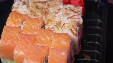Suşi plastik bir teslimat kutusunda yuvarlanır. Yakın çekim döner. İçinde taze Japon dürümleri, zencefil ve plastik bir kapta dönen wasabi olan suşi kutusu. Yemek teslimatı, paket yemek.