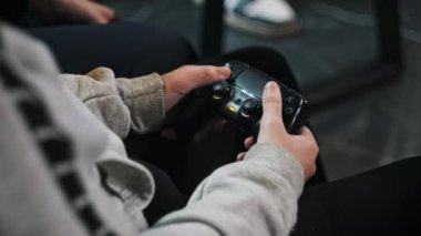 Çocuk, eğlence merkezinin oyun sahasında oyun kumandası kullanıyor. Oyun konsolunda oyun. Genç bir masada otururken elinde bir joystick 'i kontrol ediyor, yakın plan. Oyun oynayan oyuncu