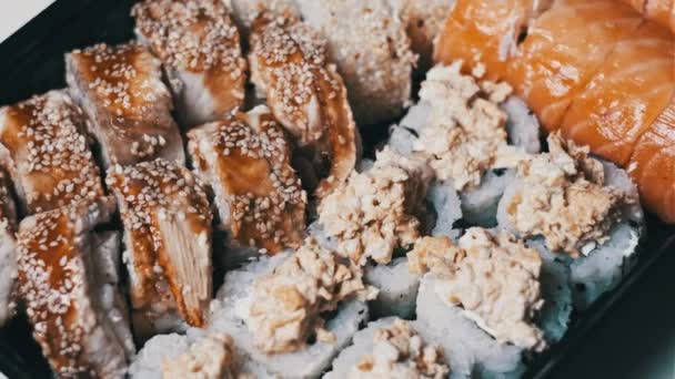 寿司卷在塑料送货箱内旋转特写 即食寿司盒与新鲜的不同口味的日本卷在一个塑料容器中旋转 食物运送概念 外卖食物 — 图库视频影像