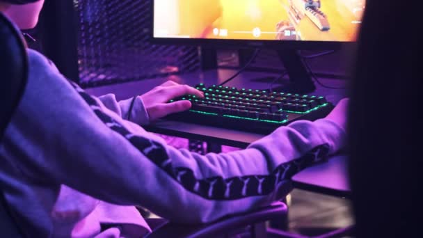 年轻的游戏玩家坐在一个专业的游戏椅子上 在电子竞技俱乐部玩电子游戏 在电脑俱乐部的耳机里 拿着霓虹灯的男孩专注于电子游戏 游戏俱乐部的青少年 — 图库视频影像