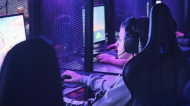 Esport kulübündeki genç bir çocuk oyun sandalyesinde monitörün önünde oturup atış oyunu oynuyor. Bilgisayar kulübünde kulaklık takan bir genç bir video oyununa odaklanıyor, arkadaşlar çevrimiçi turnuva oynuyor