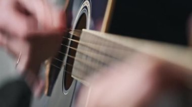 Genç adam evde akustik gitar çalar. Oturma odasında kanepede oturan müzisyen gitarı. Şarkı çalmayı öğrenmek, telleri tıngırdatmak, akorlar çalmak. Yavaş Hareket, yaşam tarzı, akıl sağlığı.