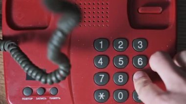 911 'i arıyorum. Eski bir kırmızı telefonun üst görüntüsü, erkek eli tuşlara basar. Eski bir ev telefonundan acil durum numarasını arıyorum. Retro tuşlu numara tuşları. Yakın plan.