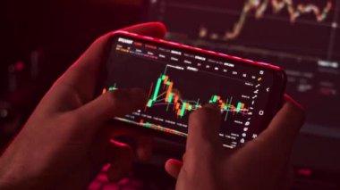 Yatırımcı cep telefonu uygulamasında kripto piyasasını kontrol ediyor. Akıllı telefon ekranındaki kripto döviz grafiğindeki BTC fiyatını analiz eden tüccar. İş adamları finansal verileri analiz ederken şifreli mobil uygulama kullanırlar