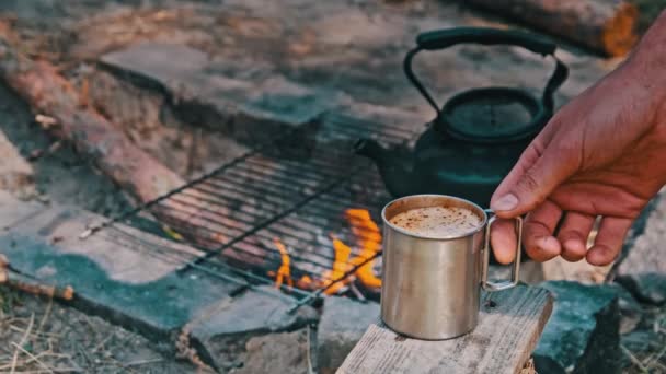 在大自然的特写镜头下 在篝火边的杯子里加入自制的香浓咖啡 由篝火酿制的带香味咖啡的游客杯 旅行者手里拿着一个刚烤好的咖啡杯 — 图库视频影像