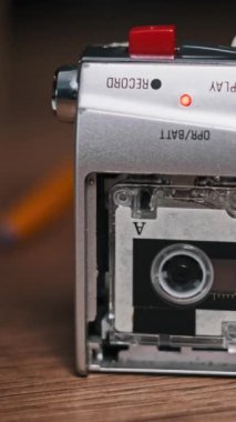 Dikey Vintage mikro kaset kaydedici ayakta dikey kayıt yapıyor. Mikro kasetin yakın çekimi ve ahşap bir masanın üzerindeki kayıt cihazındaki rulo kaset. Kaydı ara, sesi kaydet