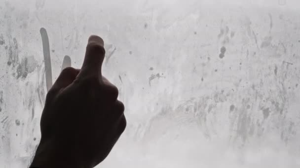 雪に覆われた背景によるガラスの凝縮窓に男性の指で描かれたWord Winter 雪の間の窓に手書きの碑文が刻まれた冬 冬の気分 テキスト — ストック動画