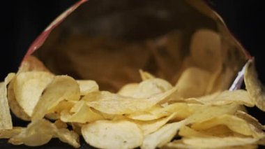 Erkek eli, siyah arka planda yakın plan patates cipsi alır. Erkek parmaklar, masada açık bir paketin yanında duran bir yığın cipsten atıştırmalık alır. Fast food, abur cubur, sağlıksız yemek yemek.