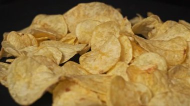 Patates cipsi siyah arka planda yakın plan çekimde döner. Masaya bir sürü çıtır cips döküldü. Makroda bir yığın kızarmış patates çerezi. Fast food, abur cubur, sağlıksız yiyecekler. 4K