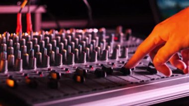 Erkek el faders yukarı ve aşağı ayarlama Neon ışık yakın çekim ses karıştırıcı. Renkli arka planda karıştırma konsolu çalışıyor. DJ çok renkli bir efekt ile müzik çalar. Ses mühendisi düğme seviyesini değiştiriyor