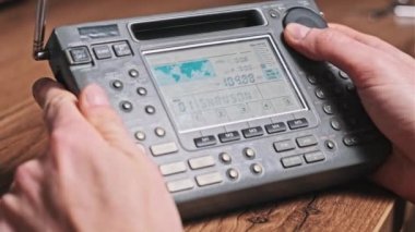 Modern Radyo ve Dijital LCD ölçekli radyo istasyonlarının insan arama frekansları. Erkek eller taşınabilir telsizi tutarak frekansı gösterir ve FM menzilini tarar. Akort alıcısı evdeki ahşap masada.