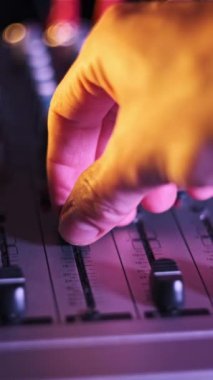 Dikey ses mühendisi faders 'ı neon ışıklı yakın plan ses mikserinde yukarı aşağı hareket ettirir. Erkek el karıştırma konsolunda ses düzeyini ayarlar. Renkli arkaplanda çalışan DJ müzik çalıyor
