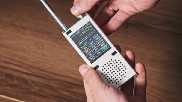ラジオ局の頻度を検索するデジタルLcdスケールの現代便利なラジオ 男性の手は 周波数とFm範囲をスキャンするポータブルラジオを保持しています 自宅の木製テーブルで受信機をチューニングする — ストック動画