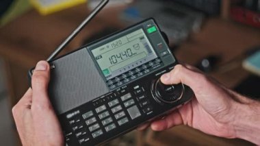 FM aralığında radyo istasyonlarının ve taramaların frekansını gösteren dijital LCD ölçeğinde modern bir telsizi elinde tutan adam. Ekranda büyük dijital parmaklı radyo alıcısı ayarlanıyor