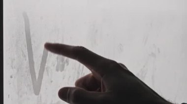 Kar yağarken sisli bir pencereden Winter 'a parmak işareti yapmak. Erkek parmağı, kar fırtınası sırasındaki bir kış günü sisli bir cama yazıyı çizer. El yazısıyla yazılmış bir metin. Kış havası