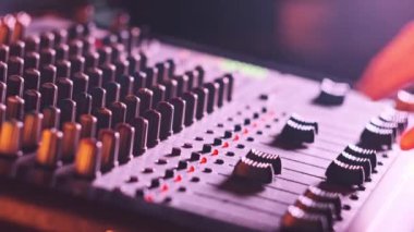 Ses mühendisi, ses karıştırıcıyı neon ışıkta yukarı aşağı hareket ettirir. Erkek el karıştırma konsolunda ses düzeyini ayarlar. Renkli arka planda çalışan DJ, müzik çalıyor