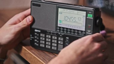Modern Radyo ve Dijital LCD ölçekli radyo istasyonlarının insan arama frekansları. Erkek eller taşınabilir telsizi tutarak frekansı gösterir ve FM menzilini tarar. Akort alıcısı evdeki ahşap masada.