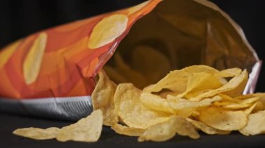 Erkek eli, siyah arka planda yakın plan patates cipsi alır. Erkek parmaklar, masada açık bir paketin yanında duran bir yığın cipsten atıştırmalık alır. Fast food, abur cubur, sağlıksız yemek yemek.