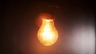 Yanan ampul açılıp kapanıyor ve siyah arkaplanda yanıp sönüyor. Metnin yeri. Isınan filament yakın plan. Cam gibi parlak sarı bir ampul. Tungsten lamba ışığı. Fikir: Boşluğu kopyala