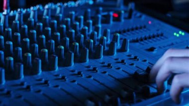 Ses mühendisi, ses karıştırıcıyı neon ışıkta yukarı aşağı hareket ettirir. Erkek el karıştırma konsolunda ses düzeyini ayarlar. Renkli arka planda çalışan DJ, müzik çalıyor