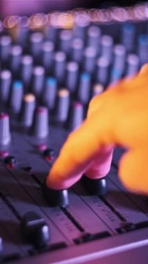 Dikey DJ el, konsol faderatörlerini neon ışıklı yakın planda karıştırmak için ses seviyesini ayarlar. Ses mühendisi ses karıştırıcıda düğmeleri aşağı yukarı hareket ettiriyor. Renkli arka planda çalışan adam müzik çalar