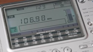 Modern Radyo ve Dijital LCD Ölçekli radyo istasyonlarının frekansları aranıyor. Erkek eller taşınabilir telsizi tutarak frekansı gösterir ve FM menzilini tarar. Akort alıcısı evdeki ahşap masada.