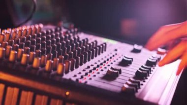 DJ el, konsol faderlarını neon ışıklı yakın planda karıştırmak için ses seviyesini ayarlar. Ses mühendisi ses karıştırıcıda düğmeleri aşağı yukarı hareket ettiriyor. Renkli arka planda çalışan adam müzik çalar