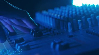 Erkek el faders yukarı ve aşağı ayarlama Neon ışık yakın çekim ses karıştırıcı. Renkli arka planda karıştırma konsolu çalışıyor. DJ çok renkli bir efekt ile müzik çalar. Ses mühendisi düğme seviyesini değiştiriyor