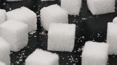 Şeker küpleri masaya yakın çekimde döner. Beyaz rafine şekerin çoğu siyah arkaplanda pürüzsüz döner. Kavramsal şeker bağımlılığı, sağlıksız beslenme, aşırı kilo, diyabet ve obezite. Boşluğu kopyala