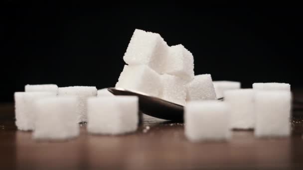 スプーン内の砂糖キューブは 黒い背景のクローズアップのテーブルの上に回転します 甘い白砂糖の山が付いている金属のスプーン 砂糖中毒 不健康な食事 過体重 糖尿病 肥満を概念する — ストック動画