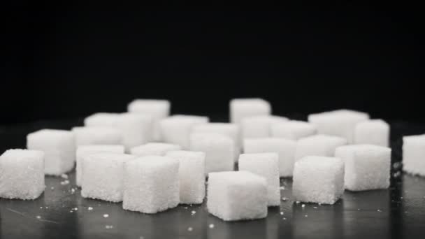 シュガーキューブはテーブルのクローズアップで回転する 白砂糖の多くは黒い背景に滑らかな回転をしています 砂糖中毒 不健康な食事 過体重 糖尿病 肥満を概念する コピースペース — ストック動画
