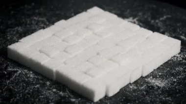 Şeker küpleri yakın çekimde döner. Birçok beyaz rafine şeker küpleri siyah bir zemin üzerinde dönen kare şeklinde katlanır. Şeker bağımlılığı, sağlıksız beslenme, aşırı kilo, diyabet, obezite. Boşluğu kopyala