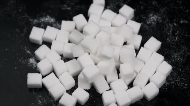 多くの砂糖キューブは黒い背景のクローズアップで回転します 白い精製された砂糖のキューブがテーブルの上に回っています 砂糖中毒 不健康な食事 過体重 糖尿病 肥満の概念 スペースをコピーする — ストック動画