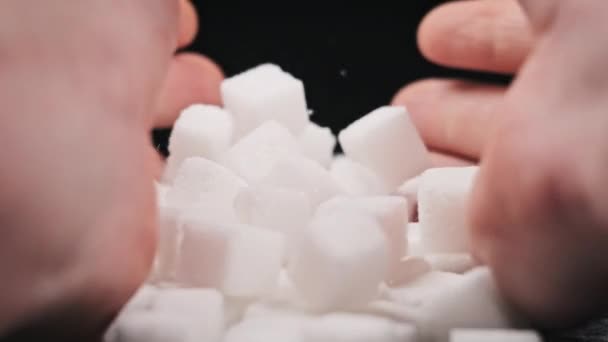 男性的手慢慢地将糖立方体弯曲成黑色桌子上的一堆 许多糖块在一张桌子上旋转 不健康饮食 糖尿病 肥胖症的概念 — 图库视频影像
