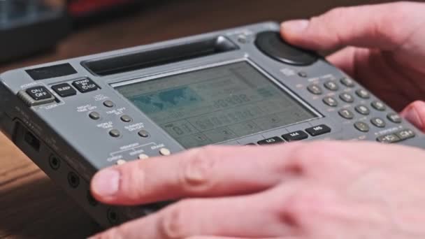 用数字液晶天平搜索现代广播电台的频率 男性手握显示频率和扫描调频范围的手提式收音机 在家里的木制桌子上调整接收机 — 图库视频影像