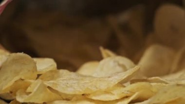 Erkek eli, siyah arka planda yakın plan patates cipsi alır. Erkek parmaklar, masada açık bir paketin yanında duran bir yığın cipsten atıştırmalık alır. Fast food, abur cubur, sağlıksız yemek yemek.