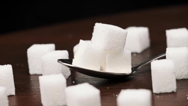 スプーン内の砂糖キューブは テーブルのクローズアップで滑らかな回転です 甘い白砂糖のヒープが付いている金属スプーン 砂糖中毒 不健康な食事 過体重 糖尿病 肥満を概念する — ストック動画
