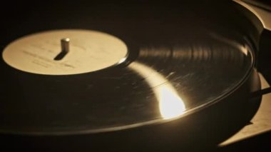 Retro turntable 'a yakın çekimde vinil çeviriyorum. Eski bir vinil kaydın eski bir plakta dönüşümlü görüntüsü. Vinil bir yüzeydeki lamba ışınının sıcak yansıması. Müzik tarihi, geçmişe dönük.
